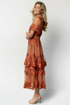 Model seated in the Lotte rust embroidered midi dress illustrating skirt drape, movement, and smocked waist detail.