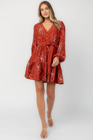 Rust floral mini dress with a V-neckline, button-front bodice, long balloon sleeves, elastic waistband with a self-tie sash, tiered ruffle hem, and side pockets.