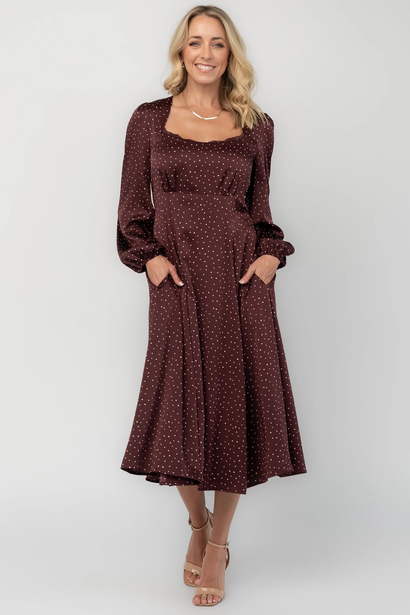 Mahogany brown midi dress with a square neckline, long sleeves, smocked back waist, removable back bow, side pockets, and a flowing skirt with heart details.