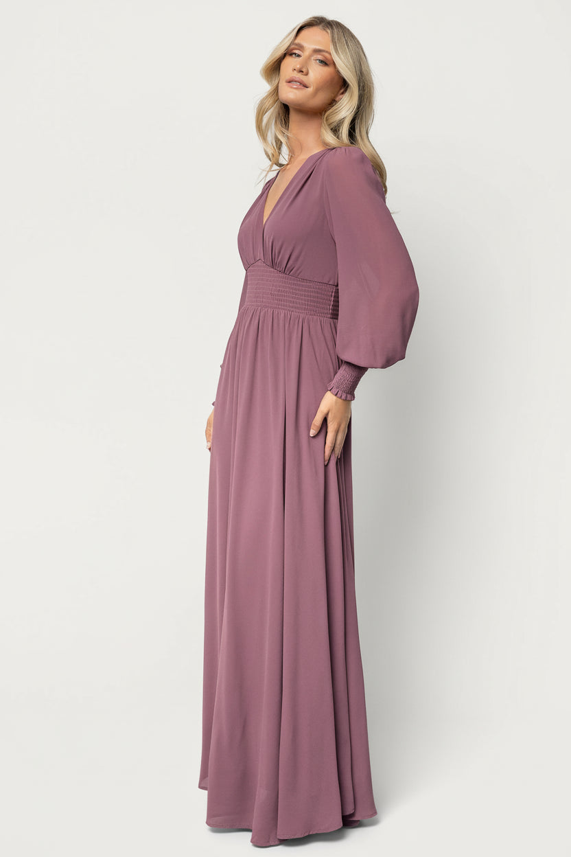 Three-quarter view of Olivia Maxi Dress in vintage plum, highlighting long sleeves, smocked waist, and overall fit on model.