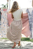 Model wearing Myra sweater dress in ivory coral floral, showing relaxed midi silhouette and rolled neckline, hands in side pockets.