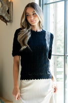 Back view of Serenity Knit Sweater Top in black on model, showing scalloped hem and overall fit with unlined crochet-knit construction.