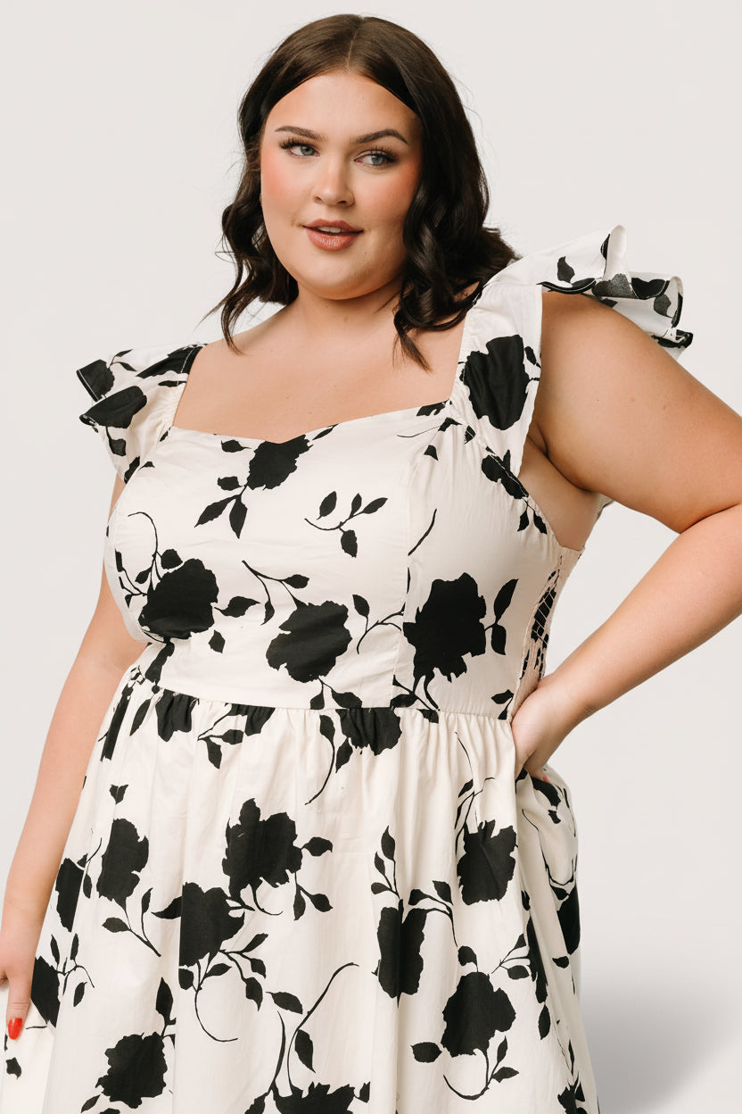 Styled flat-lay or studio shot of the ivory and black floral midi dress showing sweetheart neckline, sleeve ruffle, and A-line skirt.