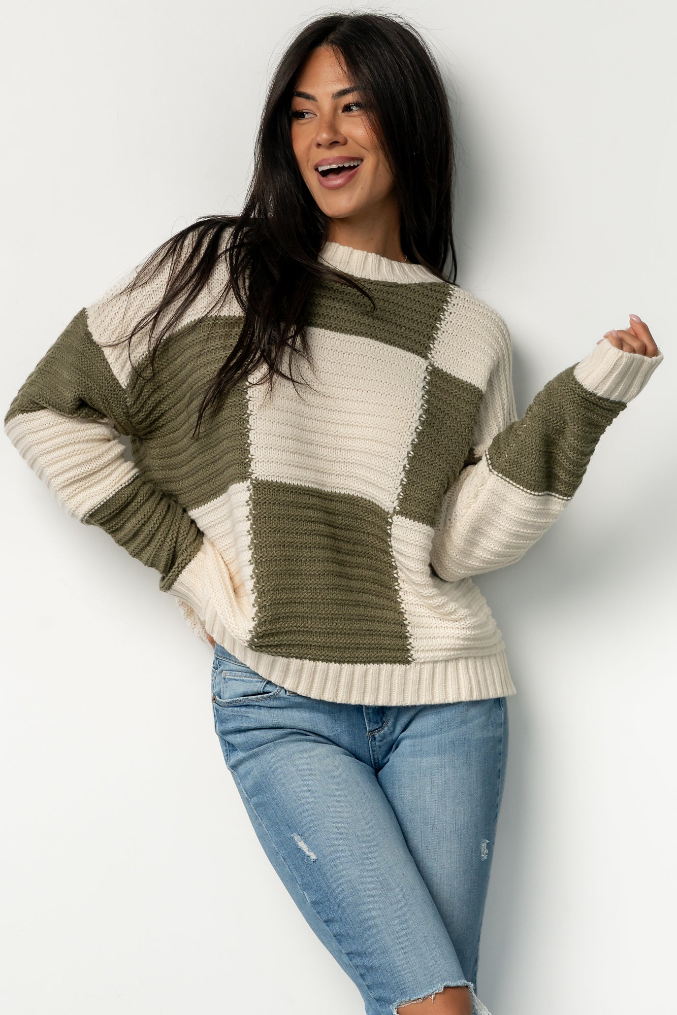 Three-quarter angle of Jayda sweater in cream and olive, highlighting check pattern, soft acrylic knit texture, and comfortable sleeve length.