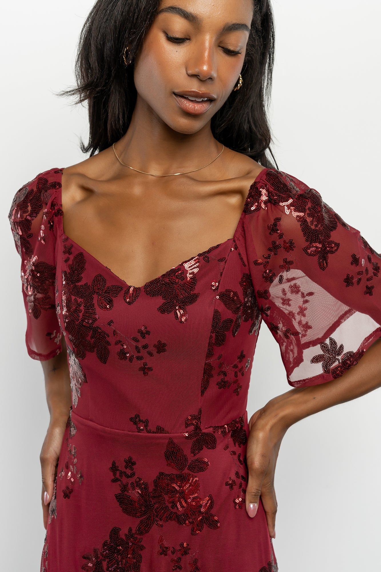 Three-quarter angle of Karina sequin maxi dress in wine showing princess seams, smocked back detail, and short sheer flutter sleeves.