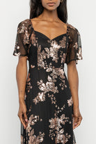 Three-quarter view of black and gold maxi dress highlighting princess seams, smocked back detail and short sheer flutter sleeve.