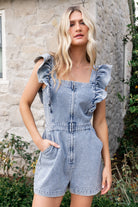 Lifestyle image of Montgomery Denim Romper in washed blue paired with casual sneakers, showing relaxed shorts, front pockets, and effortless summer styling.