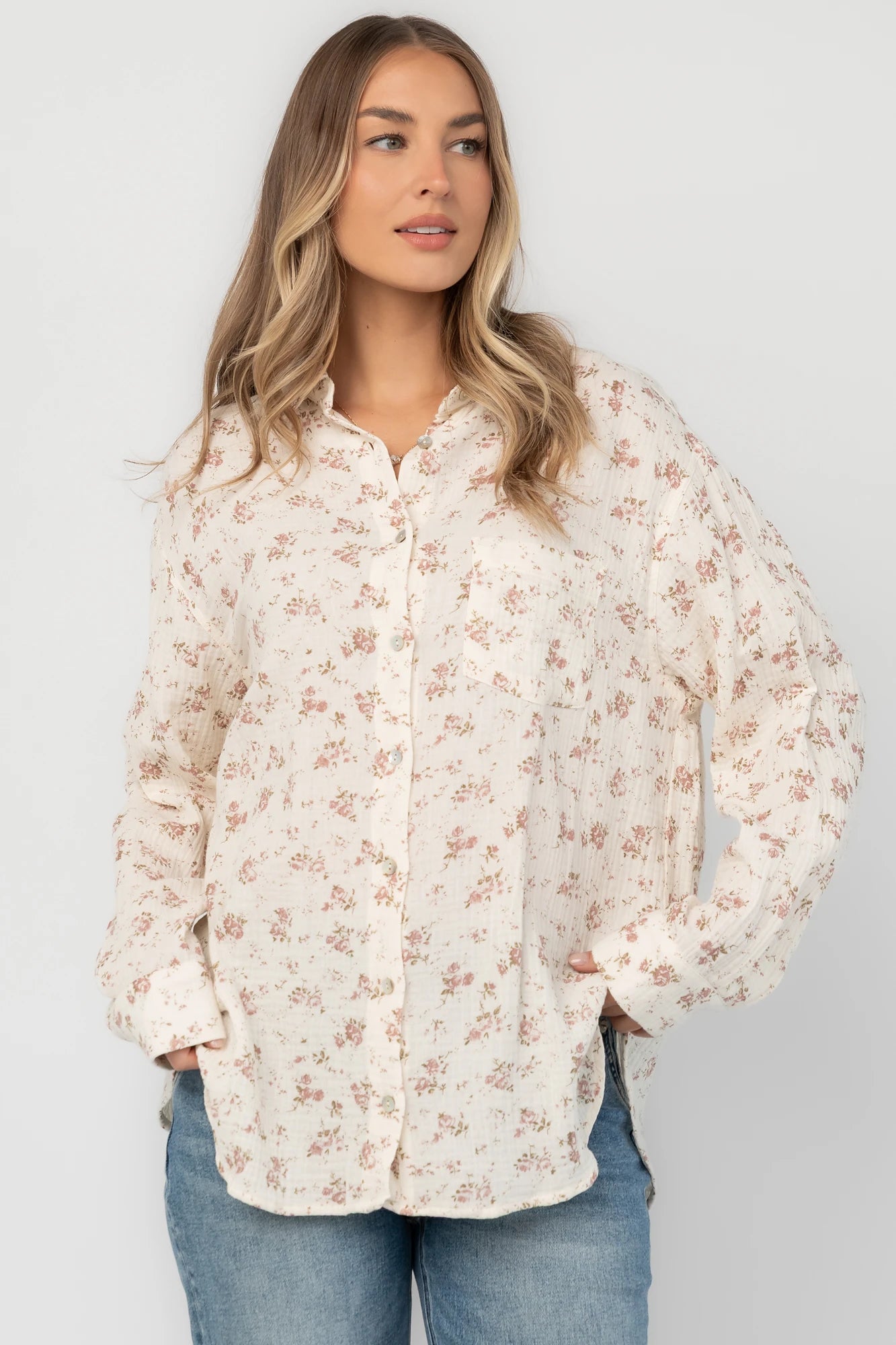Ivory floral button-front blouse with a collared neckline, long sleeves, front patch pocket, relaxed oversized fit, and rounded high-low hem.