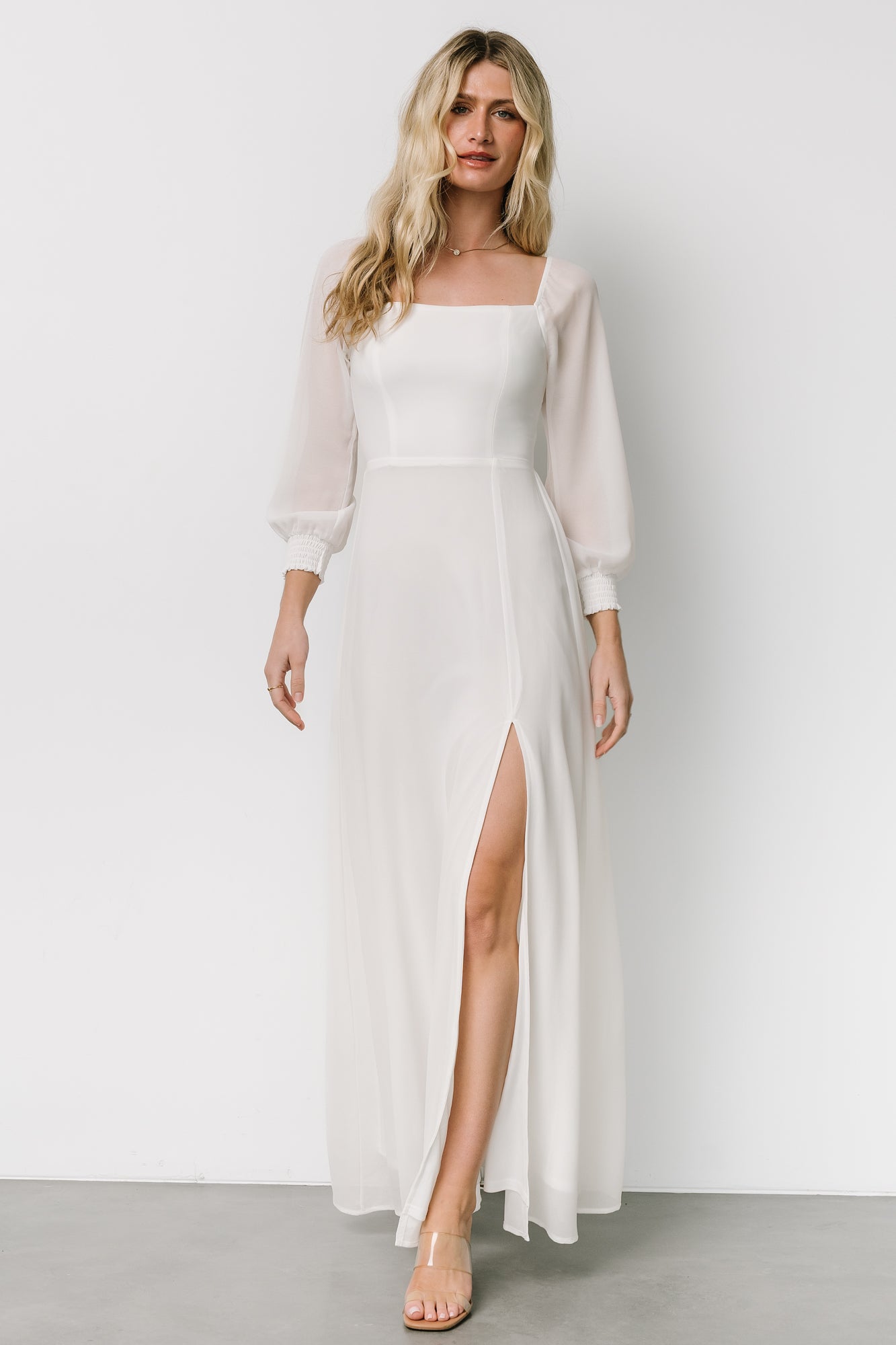 Model side view of white chiffon maxi dress showing flowing skirt, layered hem, and a left-front slit while walking.