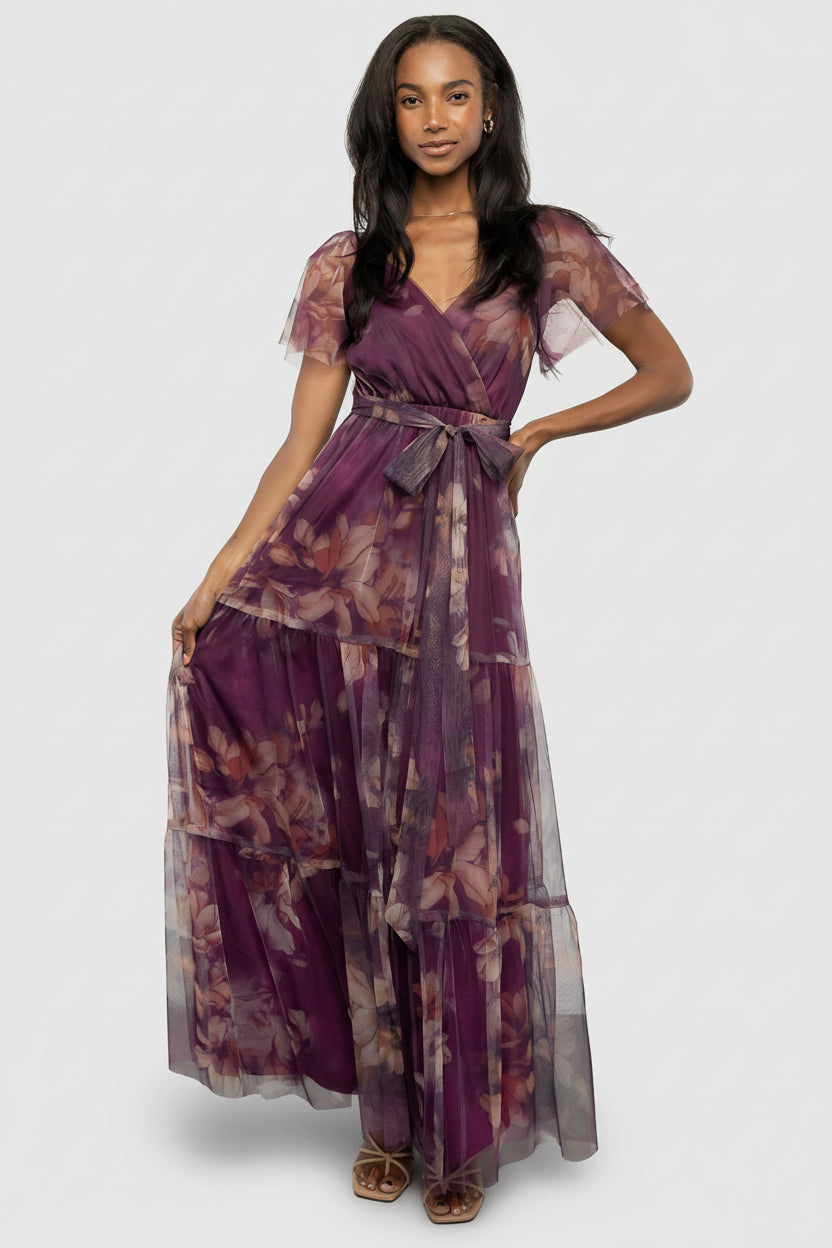 Front view of aubergine floral tulle maxi dress on a model, showing crossover surplice neckline and tiered flowing skirt in soft drape.