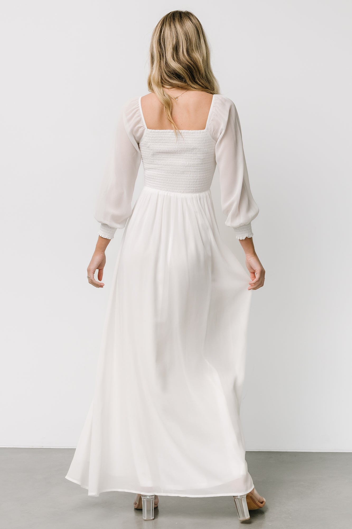 Back view of white Giselle maxi dress showing smocked back, unlined airy sleeves, and a long flowing silhouette.