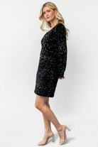 Back view of model in Mira sequin short dress highlighting back drape, full lining, and overall sequin coverage on velvet base.