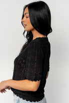 Flat-lay of the Serenity Knit Sweater Top in black showing silhouette, scalloped trim at hem and sleeves, and crochet-style holes throughout the knit.