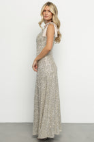 Model wearing Saya sequin maxi dress at an angle to display silhouette, neckline, and the gown's sparkling finish in champagne.