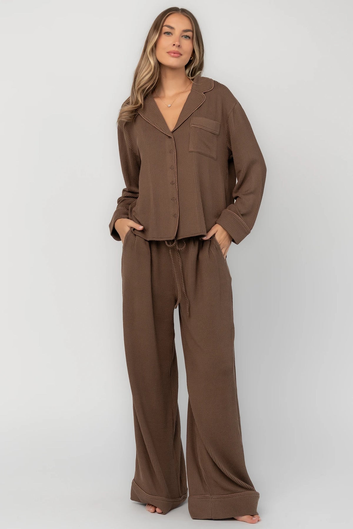 Brown ribbed pajama set with a button-front V-neck top, long sleeves, chest pocket, and wide-leg pants with an elastic drawstring waist.