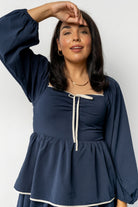 Studio image of the navy Barcelona tiered dress on model, highlighting fabric texture, tier overlap, and contrast ivory trim at sleeves and hem.