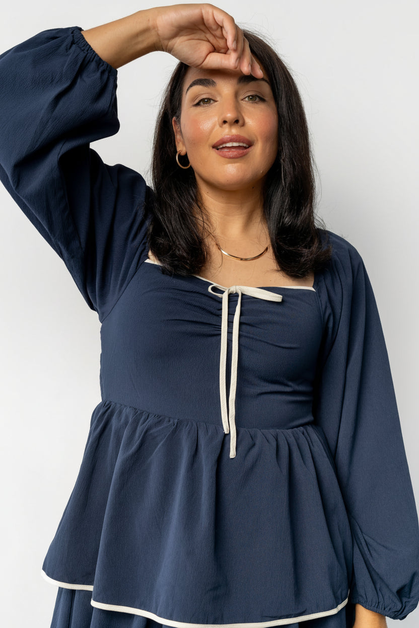 Studio image of the navy Barcelona tiered dress on model, highlighting fabric texture, tier overlap, and contrast ivory trim at sleeves and hem.