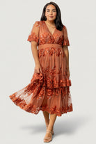Three-quarter view of the Lotte rust midi dress on model highlighting tiered ruffle overlay and flow of embroidered tulle fabric.