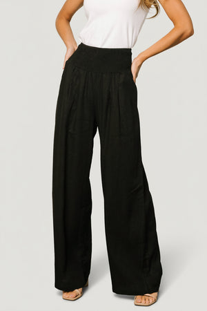 Front view of Parvati smocked high-waist wide-leg pants in black, showing smocked waistband, side pocket and fabric drape.
