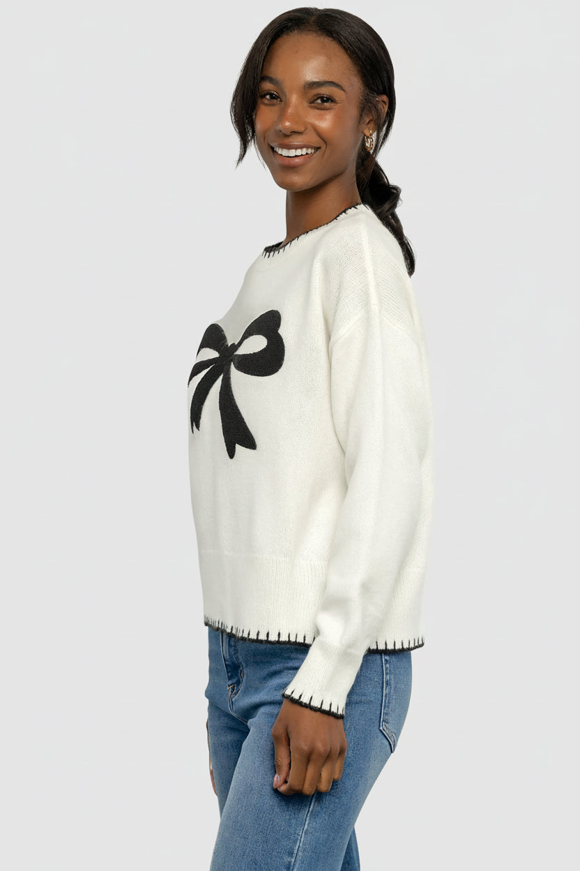 Close-up of raised decorative bow and knit texture on cream and black sweater, highlighting stitch detail and contrast piping.