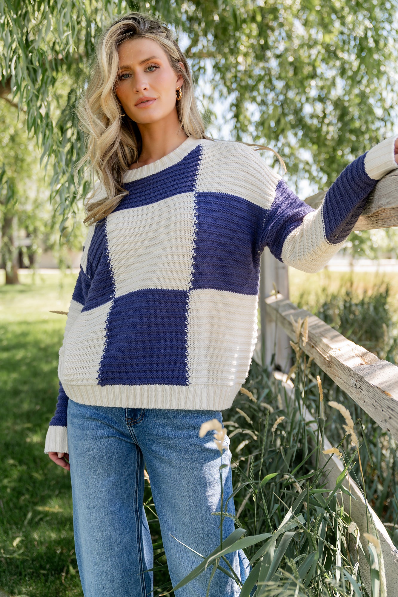 Model wearing Jayda sweater in cream and blue, front view showing checkered pattern, round neckline, and ribbed hemline.
