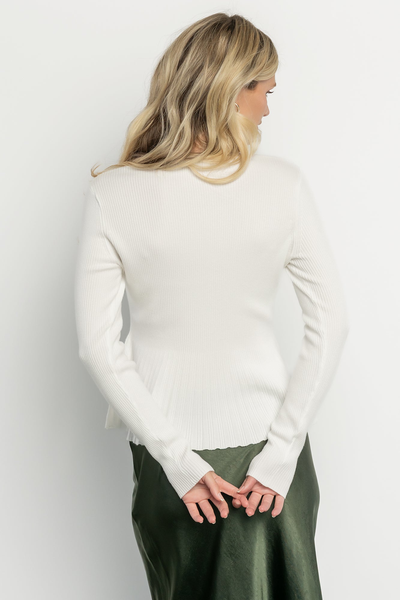 Close-up of sleeve and hem on the off-white ribbed top emphasizing stretch, texture, and the clean round neckline.