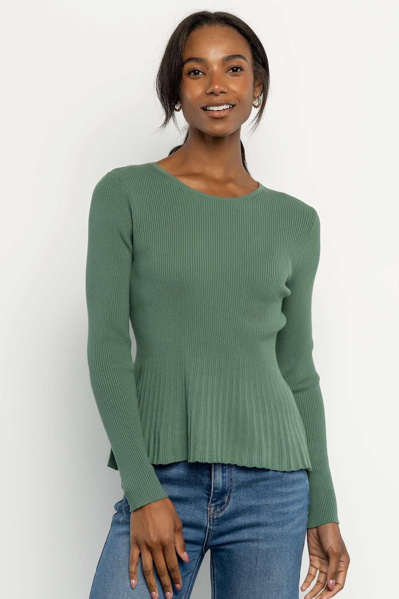 Model wearing a winter green ribbed peplum top with fitted bodice and round neckline, styled with high-rise jeans for a casual look.