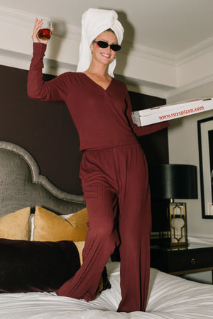 Model wearing the Rubi Soft Ribbed Pajama Set in Burgundy featuring a soft ribbed knit, long-sleeve V-neck top with a snap-button placket, and matching straight-leg pants with an elastic waistband and side pockets.