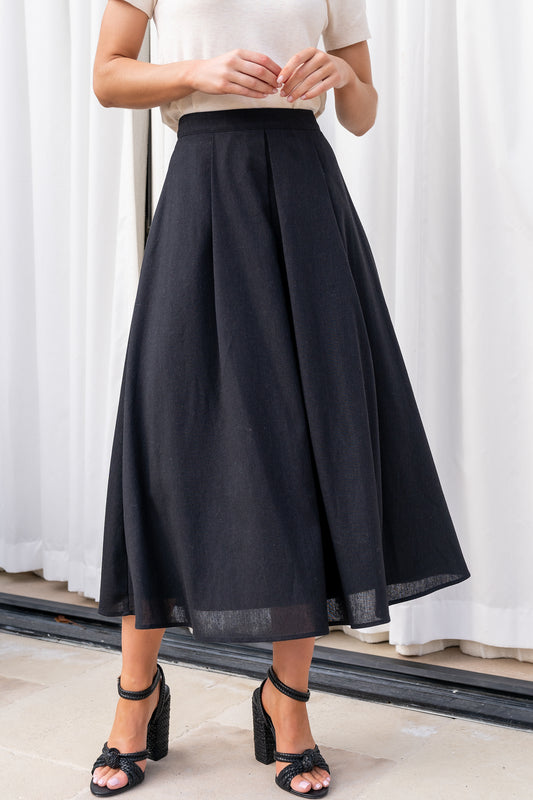 Front view of the Katie pleated midi skirt in black on a model, showing high-rise waist, defined pleats and a flowing hemline for polished movement.