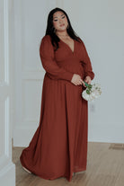 Styled image of the Olivia Maxi Dress in cinnamon paired with heels for a formal event, showcasing length, drape and sleeve cuff detail.