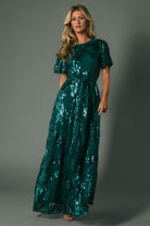 Three-quarter view of Muse Sequin Maxi Dress in emerald, highlighting short sheer sleeves, round neckline, and sequin leaf pattern across bodice.