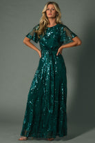 Model styling shot in Muse Sequin Maxi Dress emerald, paired with minimal accessories to emphasize sequin leaf pattern and evening wear silhouette.