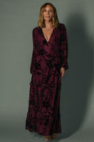 Model seated in mulberry velvet burnout maxi dress illustrating skirt movement, lined bodice, and unlined sleeves for comfort.