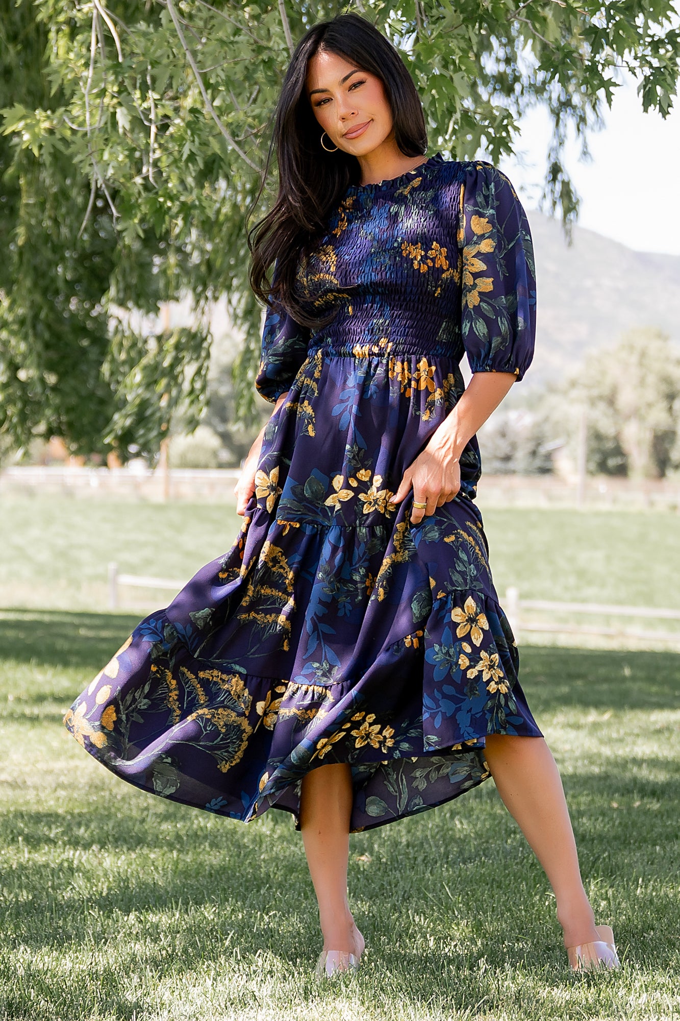 Front view of Lena Tiered Midi Dress in navy with gold floral print on a model, showing smocked bodice, ruffle collar and tiered skirt in soft chiffon.
