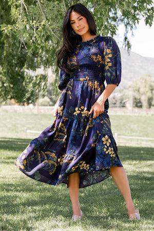 Front view of Lena Tiered Midi Dress in navy with gold floral print on a model, showing smocked bodice, ruffle collar and tiered skirt in soft chiffon.