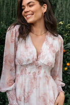 Styled flat-lay of pink floral chiffon maxi dress showing deep V-neck, smocked waist, and the white background with pink floral print.