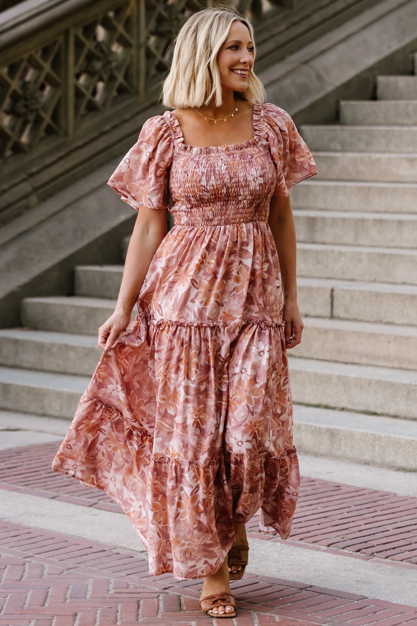 Model wearing the Southampton Smocked Maxi Dress in Dusty Mauve Floral featuring a square neckline, flutter sleeves with ruffle trim, a fully smocked bodice, and a flowing tiered maxi skirt with a dusty mauve floral print.