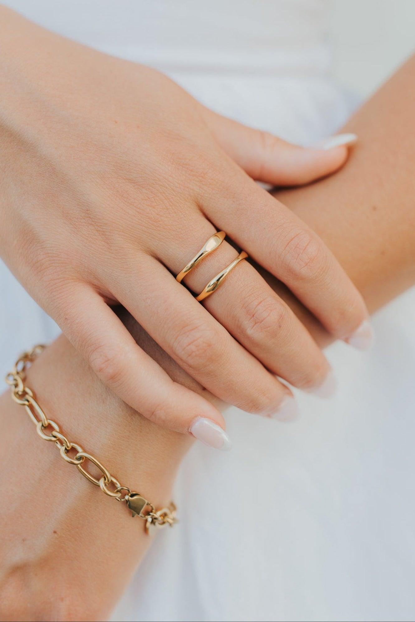 Close-up of Florence open-wave gold ring beside a bracelet on a neutral background, showing the ring's profile and polished finish.