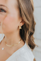 Close-up of The Sicily Hoop folded-metal gold hoop earring on white background, showing textured folded design and secure post-back closure.