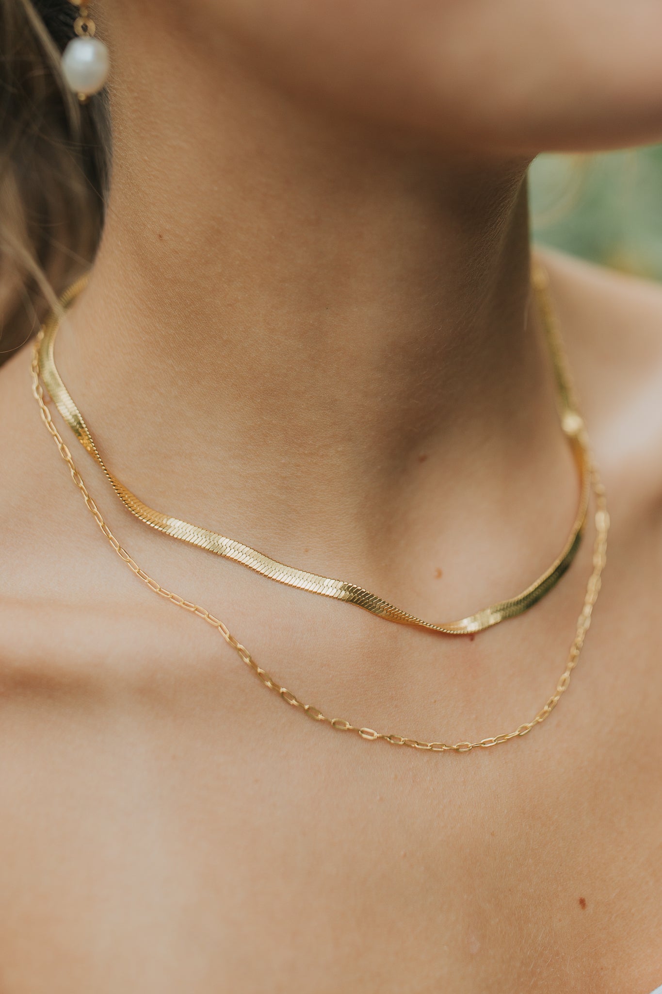 Detail shot of the necklace chains and linked clasp, highlighting the plated 18K gold finish and fine chain texture against a neutral background.