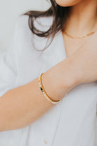 Styled flat-lay of the Lily Bracelet in 18K gold plating, emphasizing polished surface and minimalist silhouette for everyday wear.