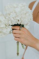 Flat lay of The Maddie ring on a neutral background showing the oval green stone and polished finish.