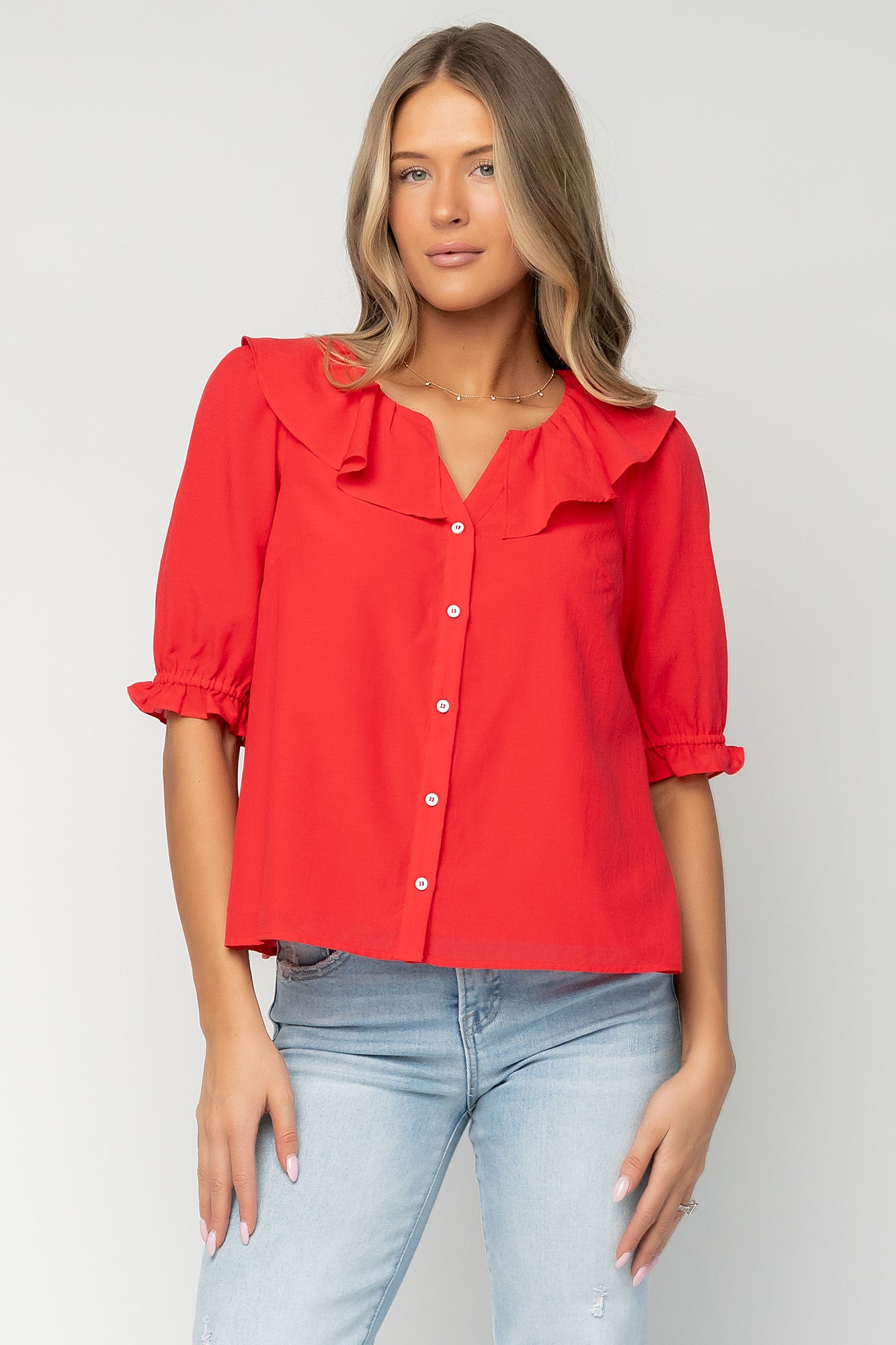 Front view of red Daisy Ruffle Button Up Top on a model, V-neck with ruffle trim, button-front, and short elastic ruffle sleeves, shown styled with jeans.