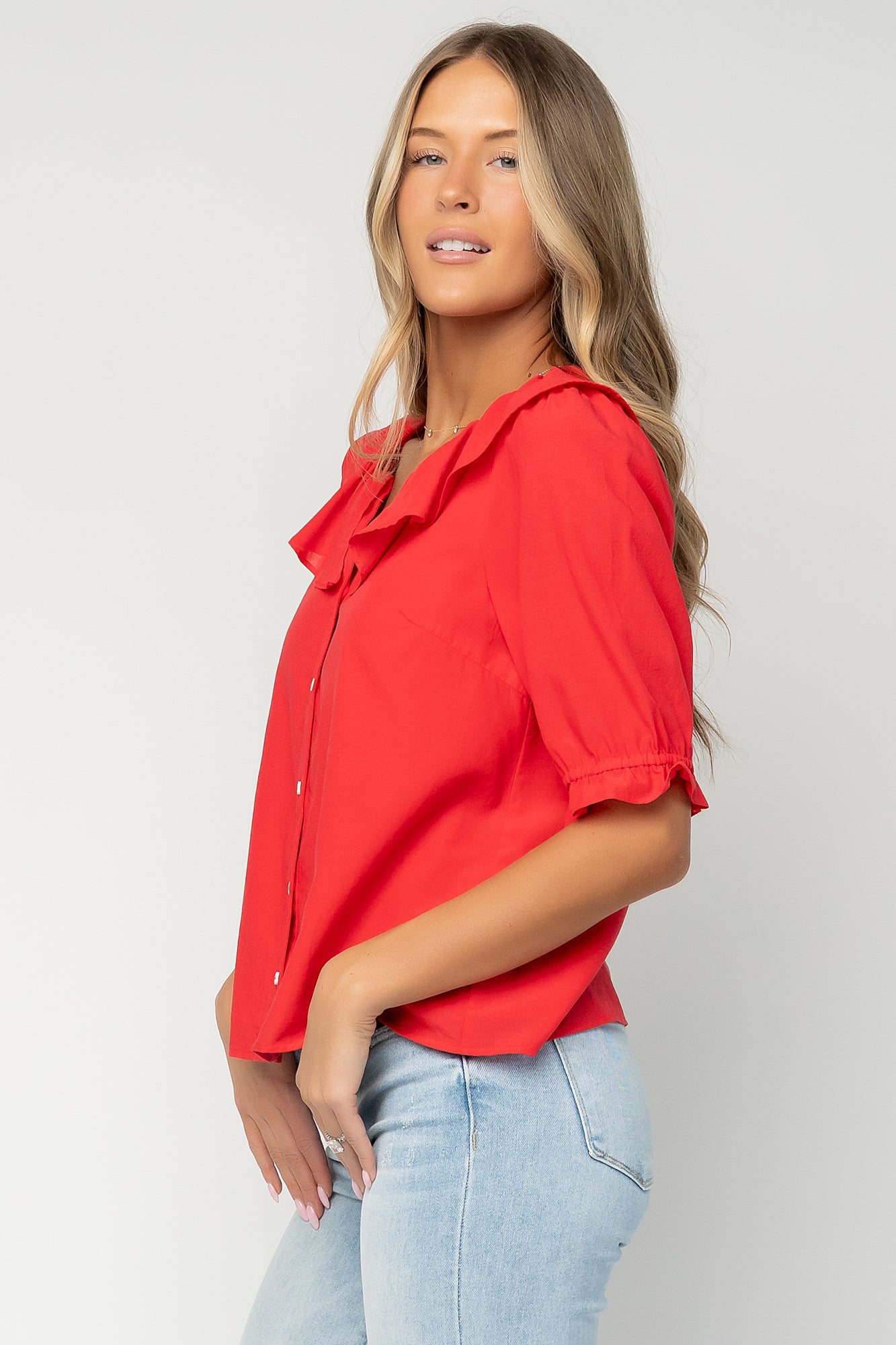 Three-quarter view of the red Daisy Ruffle Button Up Top highlighting the ruffle overlay at the neckline and the gathered elastic cuff on the short sleeve.