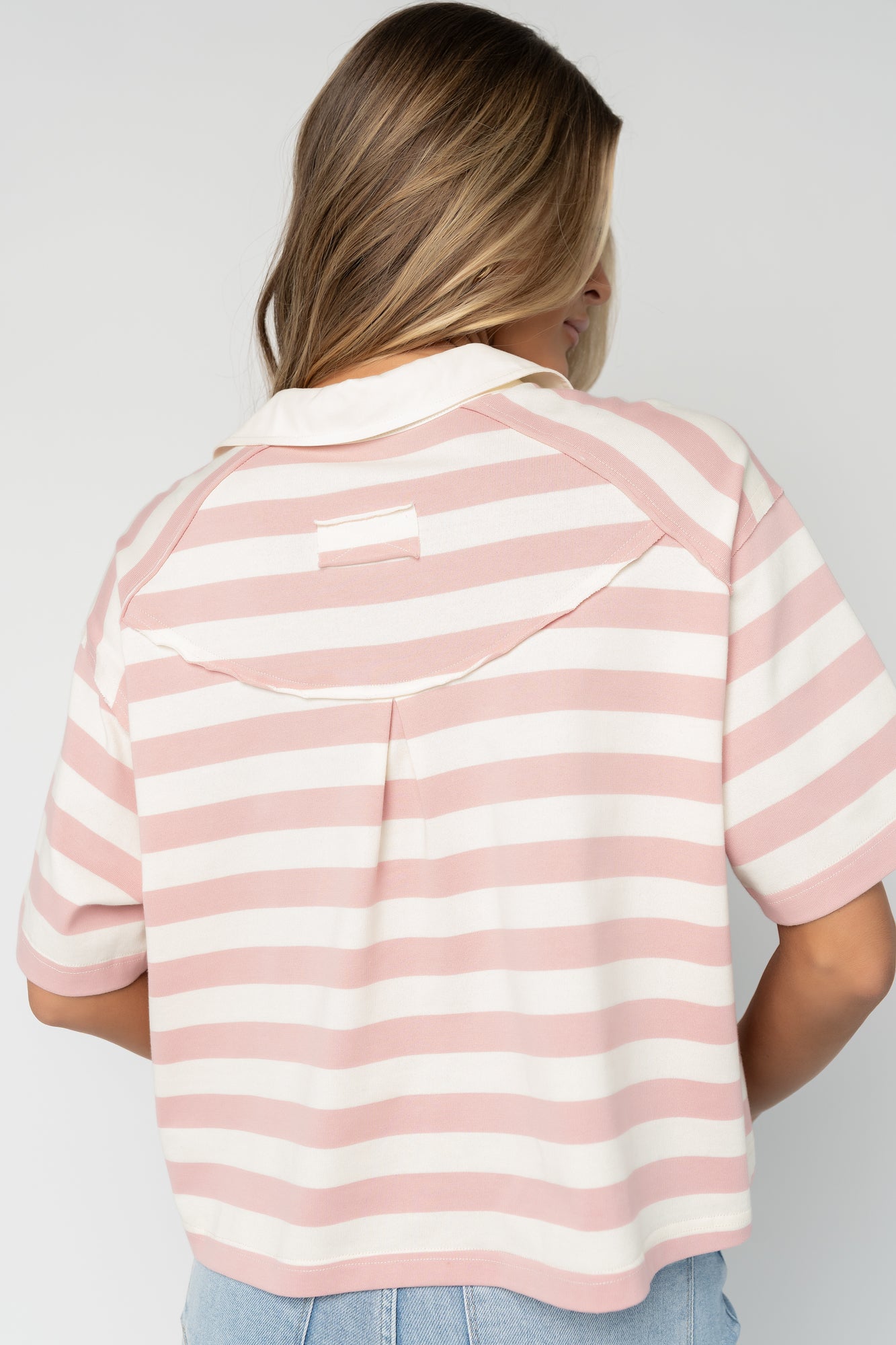 Close-up detail of the collared neckline and four functional buttons on pink and off-white striped fabric with visible texture.