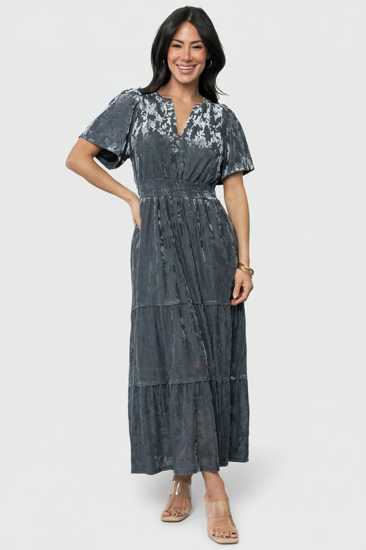 Front view of model wearing Bronwyn Velvet Dress in Dusty Blue, showing notched round neckline, flutter sleeves, smocked waistband and two-tier skirt.