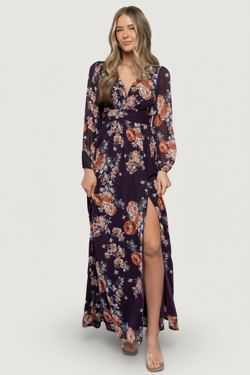Full-length front view of model wearing Adira plum floral maxi dress with V-neck, smocked back, bishop sleeves, and left leg slit, showing drape.