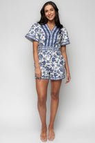 Model wearing Rafaela Romper in blue print showing adjustable V-neck with four buttons and relaxed silhouette, styled with casual accessories.