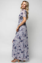 Full-length image of the dress in motion, showing the maxi-length skirt, left leg slit, and the soft dusty-lavender monochromatic floral pattern.