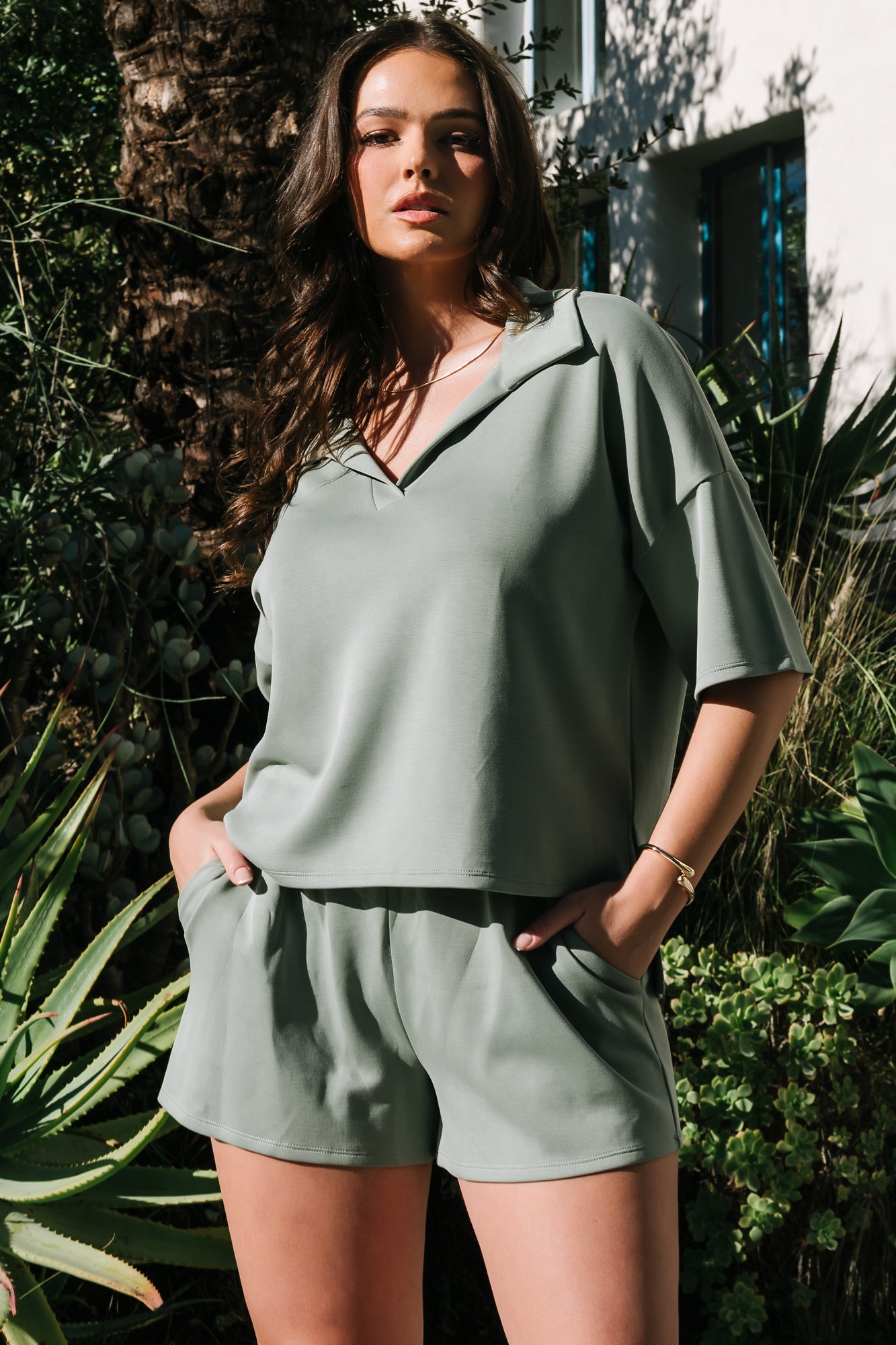 Side-angle of model in green Ana top and shorts highlighting high‑low side split hem and relaxed shorts silhouette.